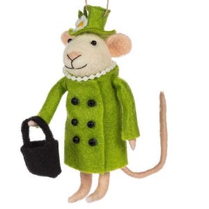 Op de afbeelding: Een vilt muis ornament, gekleed in een groene jas en hoed, met een zwarte handtas. De muis draagt een parelketting en heeft een lange, bruine staart. De hoed is versierd met een witte bloem. Een charmant decoratief stuk.