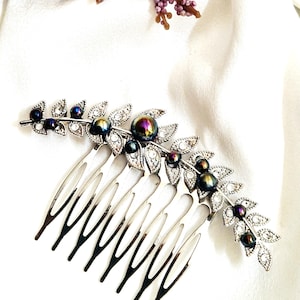 May include: Silver-toned hair comb with a leaf design. The comb features clear rhinestones and iridescent dark blue and purple beads. The leaves are detailed with small clear rhinestones. The comb is designed for formal occasions.
