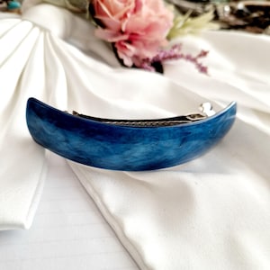 Könnte beinhalten: Eine blaue Haarklammer mit Marmoreffekt. Die Klammer ist gebogen und hat einen silbernen Metallverschluss.