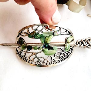 May include: Silver hair stick with a circular, openwork design featuring a tree-like pattern. The design is accented with iridescent green and blue abalone shell pieces.