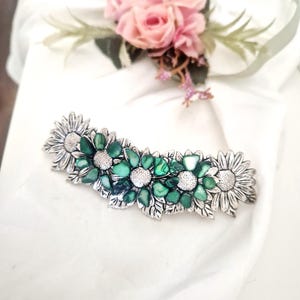 May include: A silver-toned hair clip featuring a row of five daisy-shaped flowers. The three central flowers have petals made of green shell fragments and textured silver centers, while the two outer flowers are entirely crafted from silver metal.