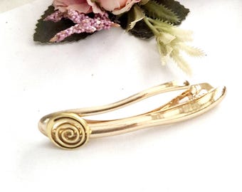 May include: A gold-toned hair clip with a spiral design. The clip is made of metal and has a smooth finish.