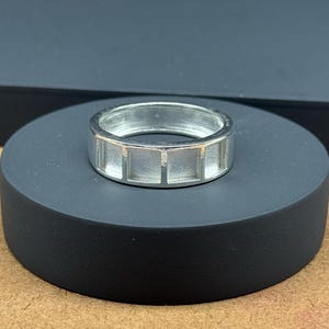 Peut inclure: Une bague en argent avec un design unique présentant une série de découpes rectangulaires autour de la bande.