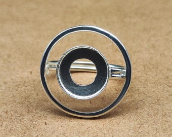 以下が含まれることがあります： ダブルサークルデザインのシルバーリング。外側の円は大きく、中央には小さく濃い色の円があります。リングはシンプルでモダンな美学を持っています。