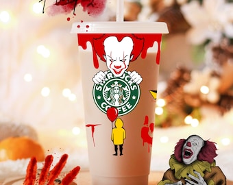 May include: A white plastic cup with a brown liquid inside. The cup is decorated with a red and white clown face, a green Starbucks logo, and a yellow character from the movie "It". There are red handprints and bloody slashes on the cup and the background.