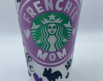May include: A white reusable cup with a purple circle that says "Frenchie Mom" and a green Starbucks logo inside. The cup is decorated with black paw prints, black silhouettes of French Bulldogs, and purple hearts.