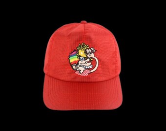 May include: A bright red baseball cap featuring a textured grid pattern on the fabric. Centered on the front panel is an embroidered graphic of a cartoon character with rainbow-colored hair, a red and white checkered shirt, and a wide grin.