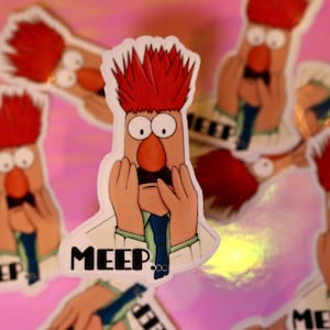 May include: A red-haired character with a surprised expression, holding their hands to their face. The character is wearing a white lab coat and a blue tie. The text "MEEP." is printed below the character.