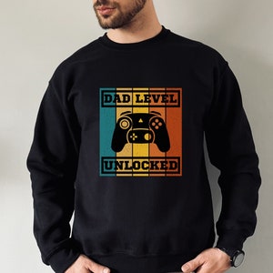 May include: Black sweatshirt with a retro-style graphic that says "Dad Level Unlocked" and features a video game controller.