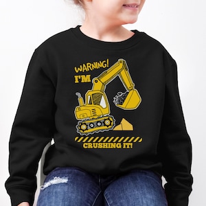 Peut inclure: Sweat-shirt noir avec un graphique d'excavatrice jaune et le texte "WARNING! I'M CRUSHING IT!"