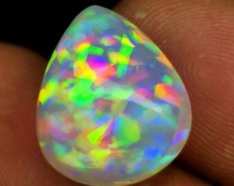 May include: A teardrop-shaped opal gemstone with a white base and iridescent flashes of green, yellow, pink, and blue.