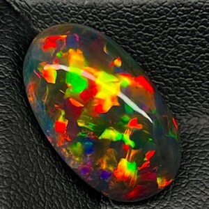 Può includere: Una pietra preziosa di opale nero con una mostra colorata di rosso, verde, giallo e blu.