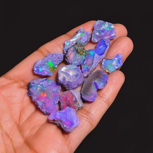 May include: A handful of raw opals, showcasing a spectrum of colors including blues, purples, greens, and reds. The opals have a rough, natural texture and exhibit a play-of-color effect, with flashes of iridescent light.
