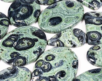 May include: A collection of polished stones in various shapes, featuring a mottled pattern of green and black. The stones have a glossy finish and are arranged on a white surface, showcasing their unique textures and colors.