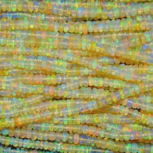 May include: Close-up of strands of opal beads. The beads are a mix of translucent white, yellow, and orange, with iridescent flashes of color. The beads are small and round, strung together.
