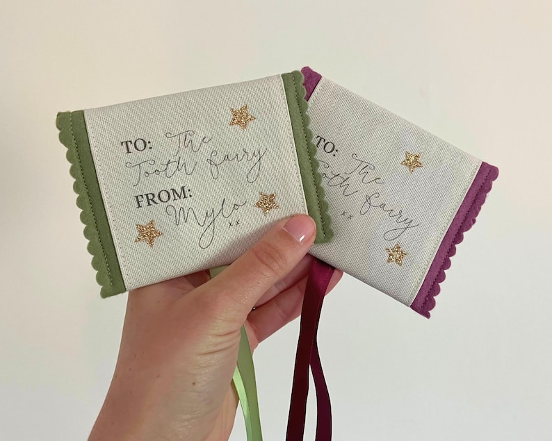 May include: Two small fabric tooth fairy pouches. One is green with a scalloped edge, the other is purple. Both have the text "TO: The Tooth Fairy FROM: Mylo" and gold glitter star accents.