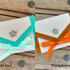 May include: Two small, decorative fabric pouches. One is mint green with a matching ribbon and the text "Mint leaf". The other is orange with a matching ribbon and the text "Pumpkin spice". Both have a star-shaped embellishment.