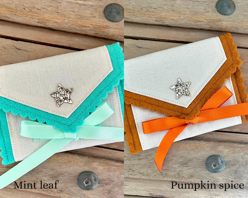 May include: Two small, decorative fabric pouches. One is mint green with a matching ribbon and the text "Mint leaf". The other is orange with a matching ribbon and the text "Pumpkin spice". Both have a star-shaped embellishment.
