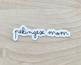 Könnte beinhalten: Ein weißer Aufkleber mit schwarzem kursivem Text, der "pekingese mom" lautet.