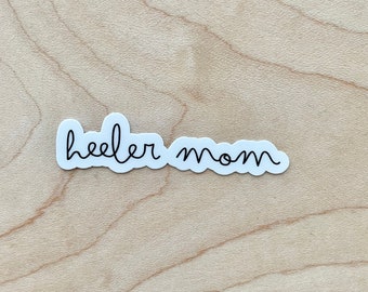 May include: A white sticker with black cursive text that reads "heeler mom".