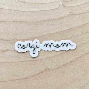 May include: White sticker with black cursive text that reads "corgi mom".