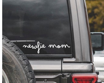 Puede incluir: Un coche negro con una calcomanía de vinilo blanco en la ventana trasera que dice "newfie mom".