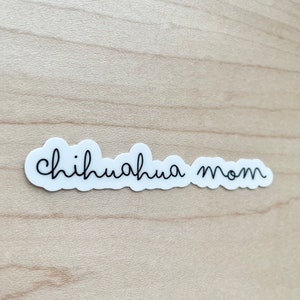 May include: White sticker with black text that reads "chihuahua mom" on a light brown wooden surface.