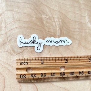 May include: White vinyl sticker with the text "husky mom" written in cursive.