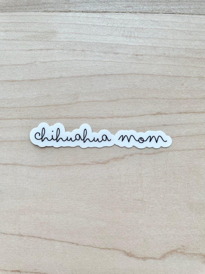 May include: White sticker with black cursive text that reads "chihuahua mom" on a light wood background.