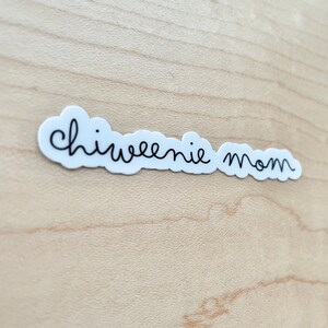 May include: White sticker with black cursive text that reads "chiweenie mom" on a light wood background.
