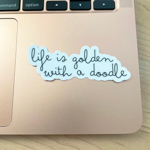 May include: A white sticker with black text that reads "life is golden with a doodle" on a gold laptop.