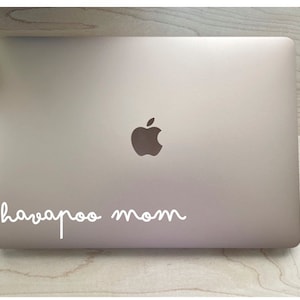 May include: A silver laptop computer with a white Apple logo and the text "havapoo mom" written in white cursive on the lid.