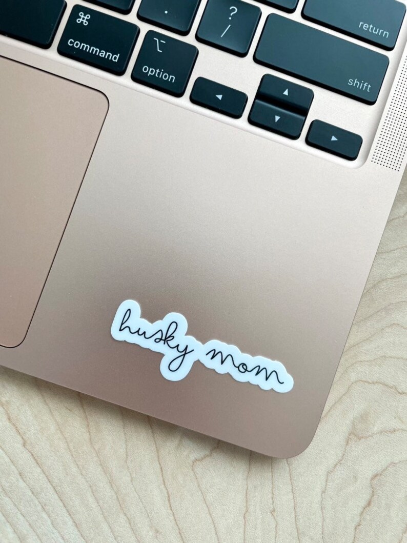 May include: White sticker with black cursive text that reads "husky mom" on a gold laptop.