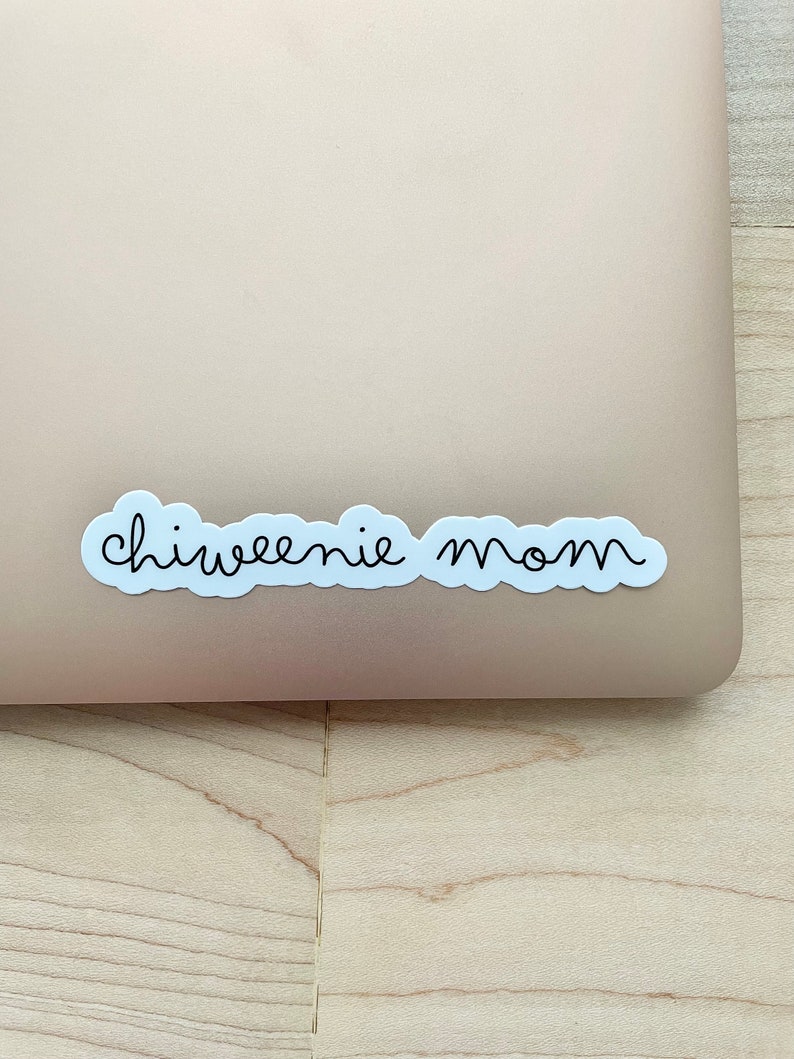 May include: A white sticker with black text that reads "chiweenie mom" on a light brown surface.