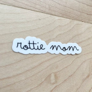 May include: White sticker with the text "rottie mom" written in black cursive.