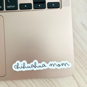 May include: A white sticker with the text "chihuahua mom" in black cursive writing on a gold laptop.