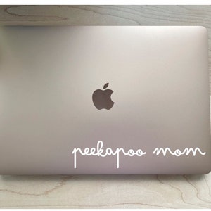 May include: A silver laptop computer with a white Apple logo and the text "peekaboo mom" written in white cursive on the lid.