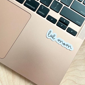 May include: A white sticker with the text "lab mom" on a gold laptop.