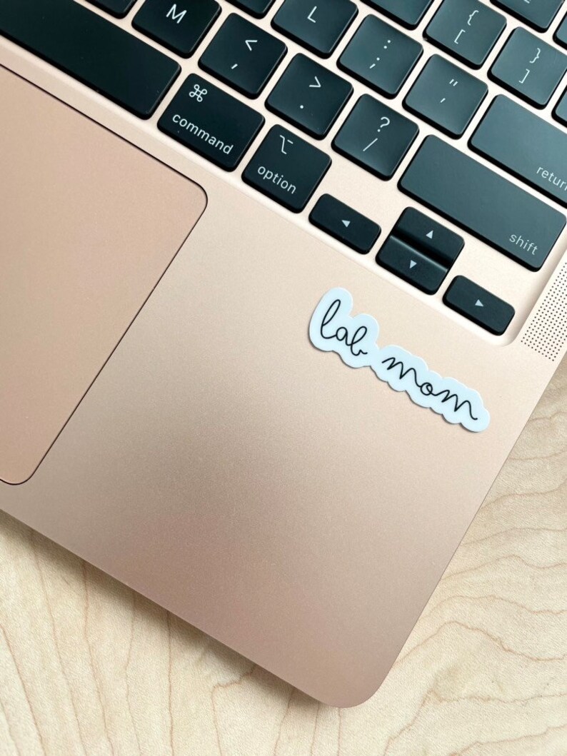 May include: A white sticker with the text "lab mom" on a gold laptop.