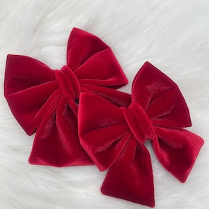 Può includere: Due fiocchi per capelli in velluto rosso. I fiocchi sono legati in una classica forma a fiocco e sono realizzati in un tessuto di velluto morbido e peluche.