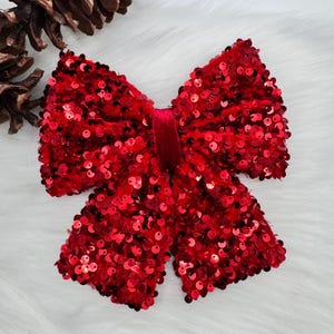 Può includere: Un grande fiocco rosso di paillettes con un centro in velluto. Il fiocco è perfetto per aggiungere un tocco festivo a qualsiasi occasione.
