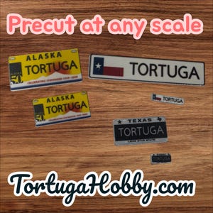 May include: Various miniature license plates with the word "TORTUGA" on them. Some plates are yellow with "ALASKA" and "50" on them. Others are white with a Texas flag design. The text "Precut at any scale" is at the top.