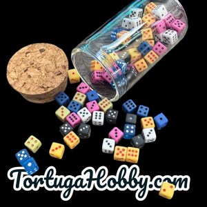 May include: A collection of colorful dice, in various colors, spilling from a clear glass jar with a cork stopper. The dice are scattered on a black background. The text "TortugaHobby.com" is at the bottom.