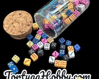 May include: A collection of colorful dice, in various colors, spilling from a clear glass jar with a cork stopper. The dice are scattered on a black background. The text "TortugaHobby.com" is at the bottom.