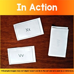 Puede incluir: Tres tarjetas blancas con letras negras sobre una superficie de madera. Las tarjetas tienen las letras "XX", "VV" y "MM" escritas en ellas. Las tarjetas son parte de un juego o actividad.