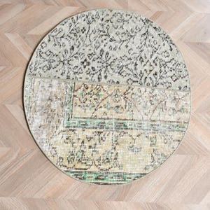 Könnte beinhalten: Ein runder Teppich mit einem Patchwork-Design aus verblassten Blumen- und geometrischen Mustern in Beige-, Hellgrün- und Schwarztönen. Der Teppich hat eine sichtbare Naht, die den oberen und unteren Bereich trennt, sowie eine Kante.