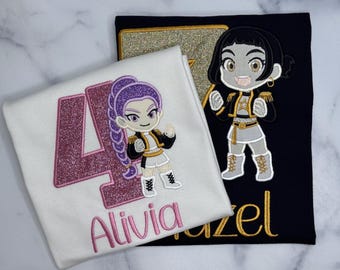 Könnte beinhalten: Ein weißes T-Shirt mit einer großen, pink glitzernden Zahl 4, dem Namen Alivia in Pink und einer gestickten Anime-Figur mit lila Haaren. Ein schwarzes T-Shirt zeigt einen goldenen Glitzerstern, eine Anime-Figur und den Namen Hazel in Gold.