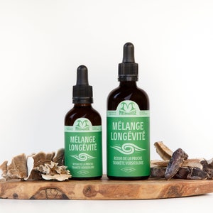 May include: Two glass bottles with droppers, both labelled "Mélange Longévité" in green text on a white background. The bottles are sitting on a wooden surface with dried mushrooms.