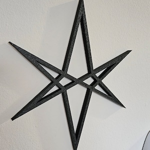 May include: A black, six-pointed star with a geometric design. The star is made of a thick, flat material and is mounted on a white wall.