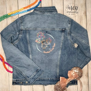 May include: A blue denim jacket with an embroidered design on the back. The design features two cartoon characters, a house, and balloons. The text "Adventure is Out There" is also embroidered on the jacket.
